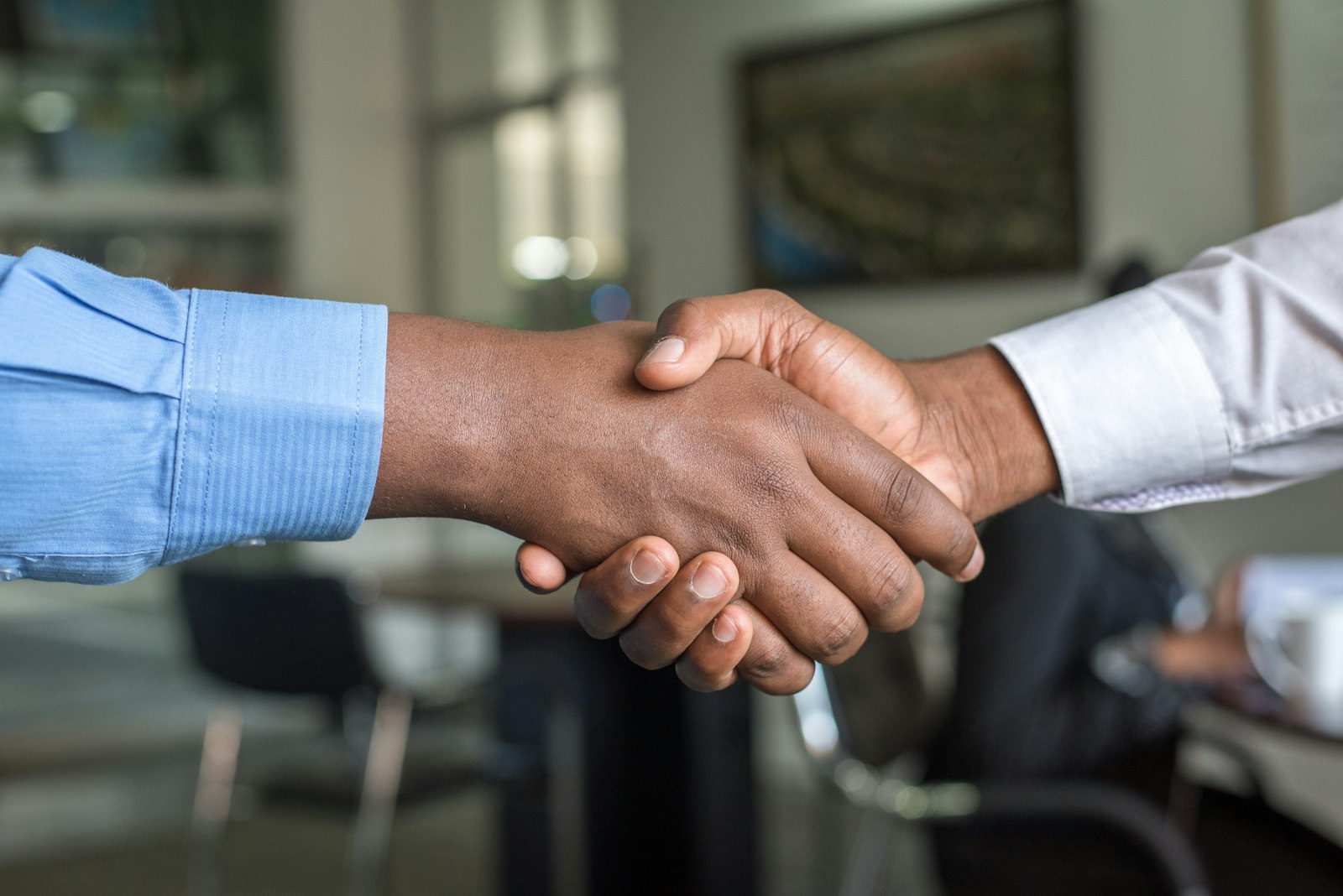 Two business people shaking hands across a table after closing a deal